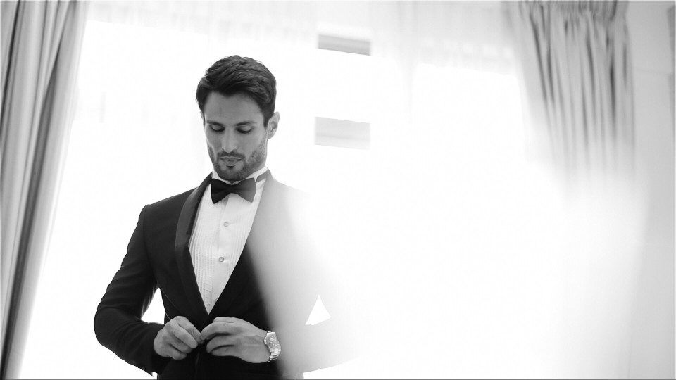 Black and white image of man buttoning suit for black tie preferred event.
