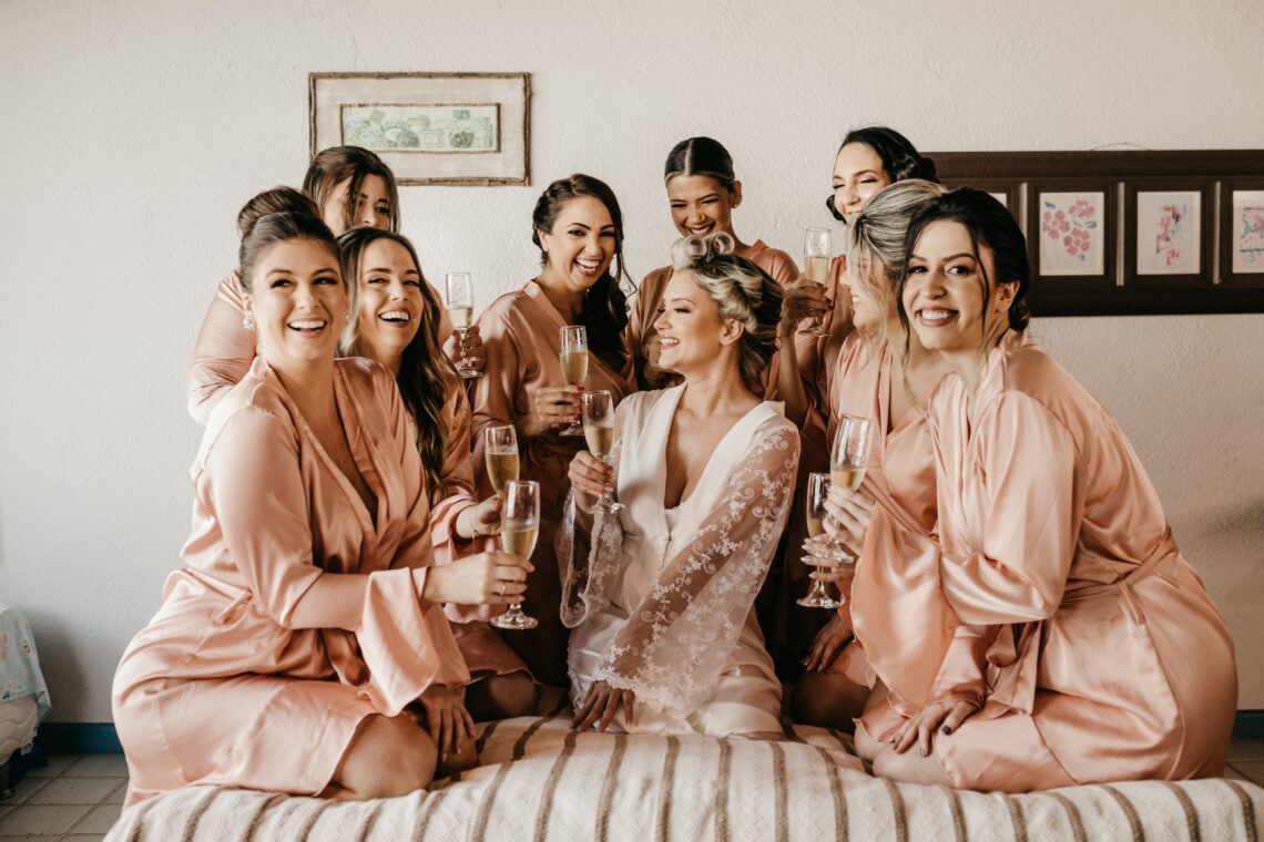 8 bridesmaids in pink robes surround bride-to-be while holding champagne flutes