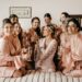 8 bridesmaids in pink robes surround bride-to-be while holding champagne flutes