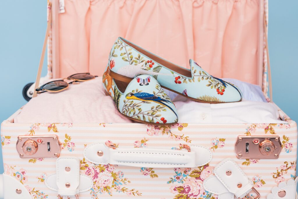 Floral suitcase with floral shoes and sunglasses packed on top. 